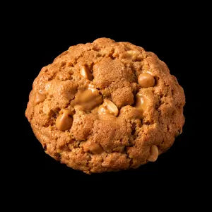 A single large golden-brown cookie with visible caramel-like chunks, photographed against a solid black background.